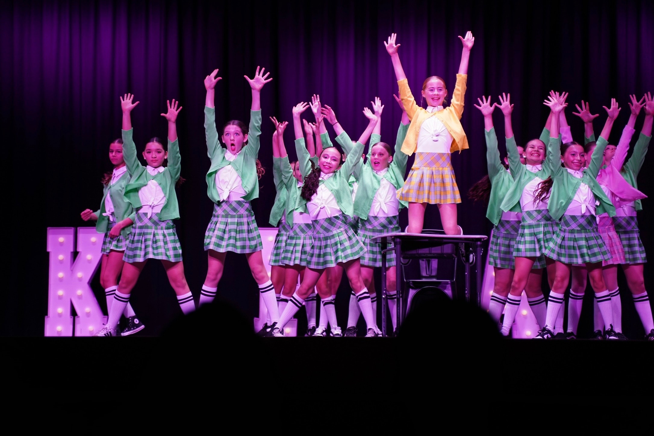 Full cast with arms raised on stage at recital